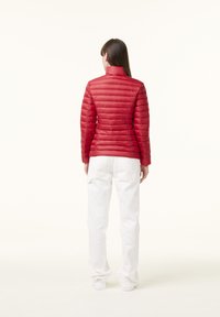 Giacca a vento rossa con design trapuntato orizzontale, colletto alto e maniche lunghe, abbinata a pantaloni bianchi dalla vestibilità comoda.