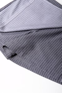 Grått stoff med tynne hvite striper, litt rynkete, som viser tekstur og mykhet. Kantene er pent sydd, noe som fremhever en skreddersydd design.