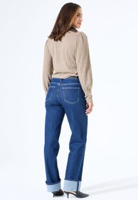 Beige strukturierter Pullover mit langen Ärmeln, kombiniert mit dunkelblauen Jeans mit umgeschlagenen Säumen und zwei Gesäßtaschen, getragen mit schwarzen Absätzen.