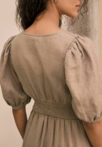 Robe à manches bouffantes en lin beige avec une taille froncée. Le tissu est doux et texturé, avec un col rond et des coutures simples.