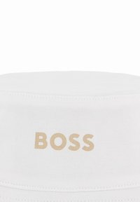 Chapeau en tissu blanc avec le mot « BOSS » imprimé en lettres beige centrées sur le bandeau avant du chapeau.