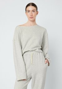 Ensemble de loungewear en coton doux et gris clair, avec un col large, des manches longues et une taille élastique avec cordon de serrage. Tissu texturé, coupe décontractée.