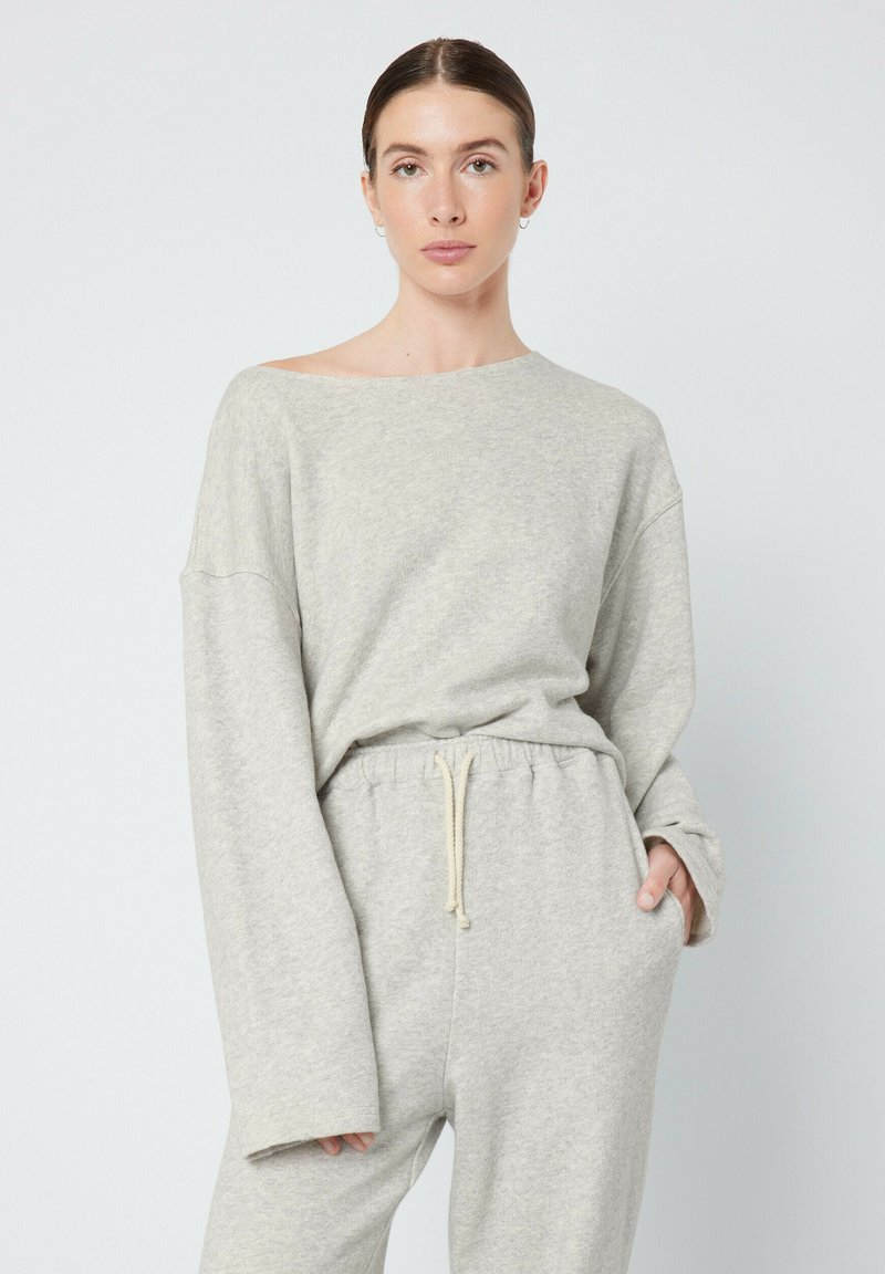 Ensemble de loungewear en coton doux et gris clair, avec un col large, des manches longues et une taille élastique avec cordon de serrage. Tissu texturé, coupe décontractée.
