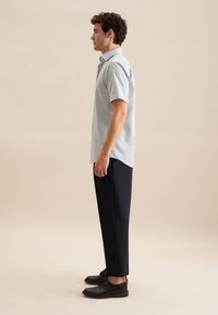 Blauw-wit gestreepte kortarmige shirt, gecombineerd met op maat gemaakte zwarte broek en zwarte veterschoenen, gepresenteerd tegen een neutrale achtergrond.