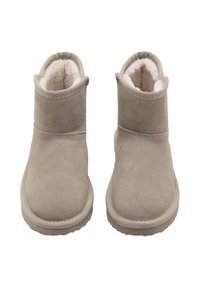 Botas de tobillo beige hechas de suave ante con un forro blanco de felpa, con una punta redondeada y una suela de goma plana.