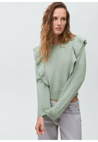 Svetlo zelena jopica z nabranimi ramenskimi detajli, rebrastimi manšetami in sproščenim krojem, v kombinaciji s sivimi denim hlačami.