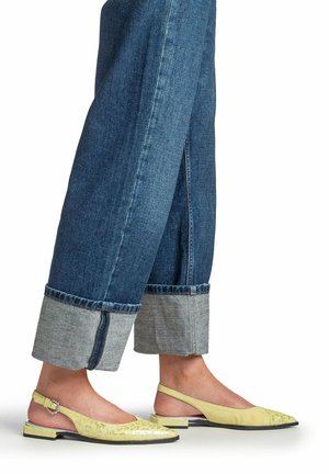 Benen in opgerolde blauwe jeans, met bleekgele slingbacks met lage hak en een subtiel bloemmotief.