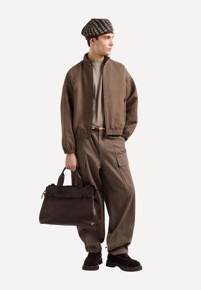 Giacca bomber in tessuto marrone, t-shirt beige, pantaloni cargo larghi color oliva, borsa in pelle marrone scuro con tracolle, berretto a fantasia, scarpe scure.