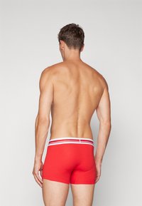 Røde boxershorts med tett passform, med en hvit midjebånd med to røde striper. Glatt bommateriale. Ingen mønstre eller tillegg detaljer.