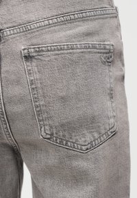 Κοντινή λήψη ανοιχτό γκρι τζιν τζιν με την πίσω τσέπη και λεπτομερή ραφή στην υφή του υφάσματος.