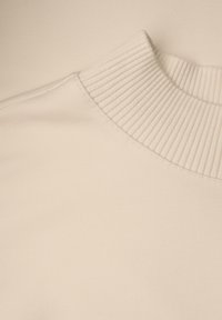 Pull beige avec col montant côtelé, texture lisse et tissu doux. Gros plan sur les coutures et le détail du col.