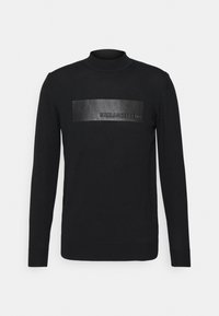 Svart långärmad polotröja gjord av mjukt material, med en matt svart läderpatch som har det präglade "KARL LAGERFELD" logot.