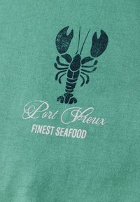 Zelená tkanina s černou grafikou humra nad textem "Port Fleux" a "Finest Seafood" v bílé, kurzívou a tučným písmem.