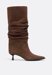 Bottine en daim marron au design décontracté, bout pointu et talon bas structuré. Texture lisse avec des plis subtils.