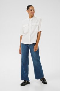 Chemise blanche à manches courtes avec un devant bouton et deux poches poitrine, assortie à un jean en denim bleu à jambes larges et des mocassins noirs.