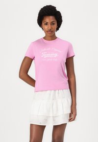 Pink short-sleeve t-shirt featuring white printed text reading "Authentic Original Tommy New York City." Soft cotton fabric, relaxed fit.