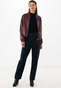 Giubbotto bomber in ecopelle bordeaux con zip dorata, dolcevita nera, jeans neri larghi con dettagli in bottone e stivaletti neri con tacco.