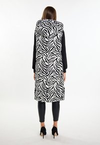 Polstret vest med et sort og hvidt zebra-stribet mønster, der har hætte og sidelommer, parret med sorte tætsiddende bukser.