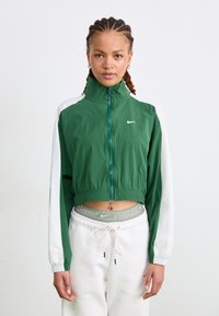 Veste verte courte avec un col haut, des manches blanches et une fermeture éclair. Présente un logo discret sur la poitrine et un ourlet élastique.