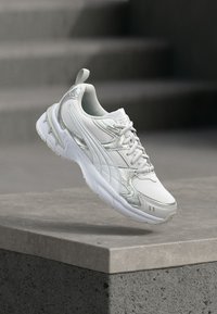 Άσπρο και ασημί αθλητικό παπούτσι αιωρείται πάνω από μια τσιμεντένια άκρη με θολές πέτρινες σκάλες στο φόντο.