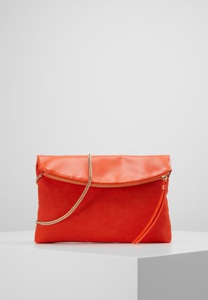 Oranje clutch met overklappende ritssluiting aan de bovenkant, gouden kettingriem en oranje ritstrekkertje, geplaatst op een wit voetstuk tegen een effen achtergrond.