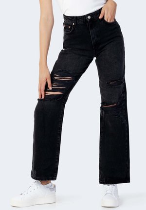 Jeans in denim nero con vita alta, vestibilità a gamba larga e diversi strappi. Abbinati a sneakers bianche con zeppa.