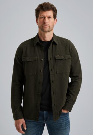 Olive green shirt jacket made of textured fabric, featuring a button-up front, two chest pockets, and button cuffs. Worn over a black shirt.