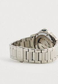 Metal link wristwatch band with clasp and partially visible watch back showing internal mechanical components.