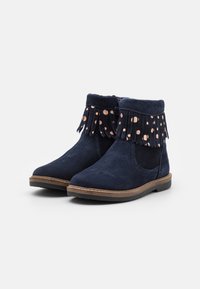Bottes de cheville en suède bleu marine avec garniture à franges et accents de pois cuivrés. Présentent un bout arrondi et une semelle en caoutchouc durable.