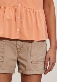 Top in cotone pesco con vita arricciata, bottoni bianchi, abbinato a pantaloni corti in cotone marrone chiaro con risvolto e tasche frontali.