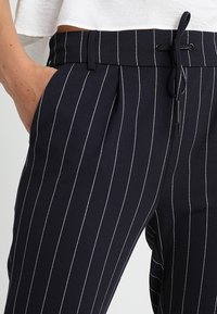 Granatowe spodnie w paski wykonane z lekkiego materiału, z elastycznym paskiem w talii i sznurkiem oraz bocznymi kieszeniami.