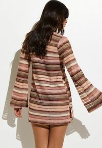 Vestido mini de punto con un patrón de zigzag multicolor en tonos rosa, marrón y crema, con mangas acampanadas y aberturas laterales.