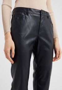 Pantalons en cuir synthétique noir avec une texture lisse, design ajusté, fermeture à bouton et poches avant, présentés au niveau de la taille.