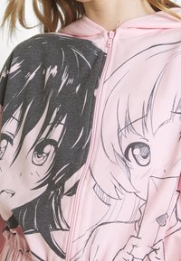 Felpa rosa con zip caratterizzata da una stampa grafica di due personaggi, uno con i capelli scuri e l'altro con i capelli chiari, su uno sfondo grigio.