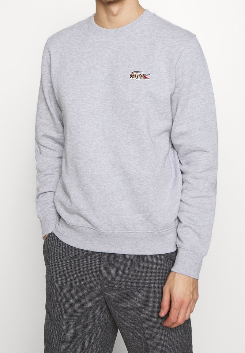 Felpa grigia chiara realizzata in un misto cotone con colletto rotondo, polsini a costine e un piccolo logo di coccodrillo ricamato con motivo leopardato.