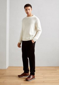 Suéter blanco de punto, pantalones de pana negros y zapatos de cuero marrón. Diseño sencillo con puños acanalados y un escote redondeado.