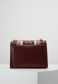 Bolso de cuero burdeos con forma estructurada, que cuenta con una correa de cadena dorada y una parte superior a rayas en tonos rosa, blanco y-beige.