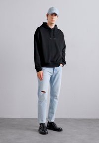 Black hooded sweatshirt, light blue ripped jeans, and black shoes. The cap is denim, complementing the casual outfit. Simple design and fit.
