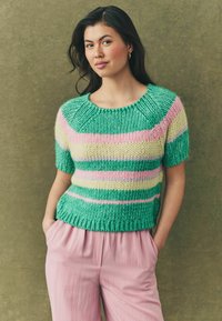 Strikket sweater med striber i grøn, pink og gul, med rund halsudskæring og korte ærmer, parret med lyserøde, afslappede bukser.