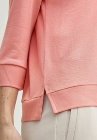 Maglione rosa chiaro con polsini e orlo a costine, dotato di spacchi laterali per una maggiore libertà di movimento, realizzato in un morbido tessuto testurizzato.