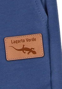 Blaues Gewebe mit einem strukturierten Lederpatch, das die Silhouette einer Eidechse zeigt und in Braun "Lagarto Verde" geprägt ist.