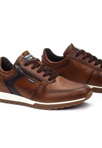 Sneakers in pelle marrone con dettagli neri, punta rotonda e suola bianca. Le caratteristiche includono lacci, un dettaglio con zip e lati testurizzati.
