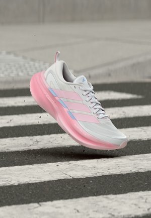 Chaussure de course blanche et rose flottant au-dessus d'un passage piéton avec des particules de terre sous la semelle sur une route en asphalte.