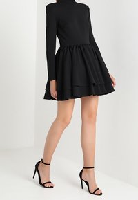 Musta pitkähihaisinen mekko, jossa on tiukka yläosa ja levenevä kerroksellinen hame. Valmistettu tekstuurikankaasta. Yhdistetty mustiin remmikenkiin.