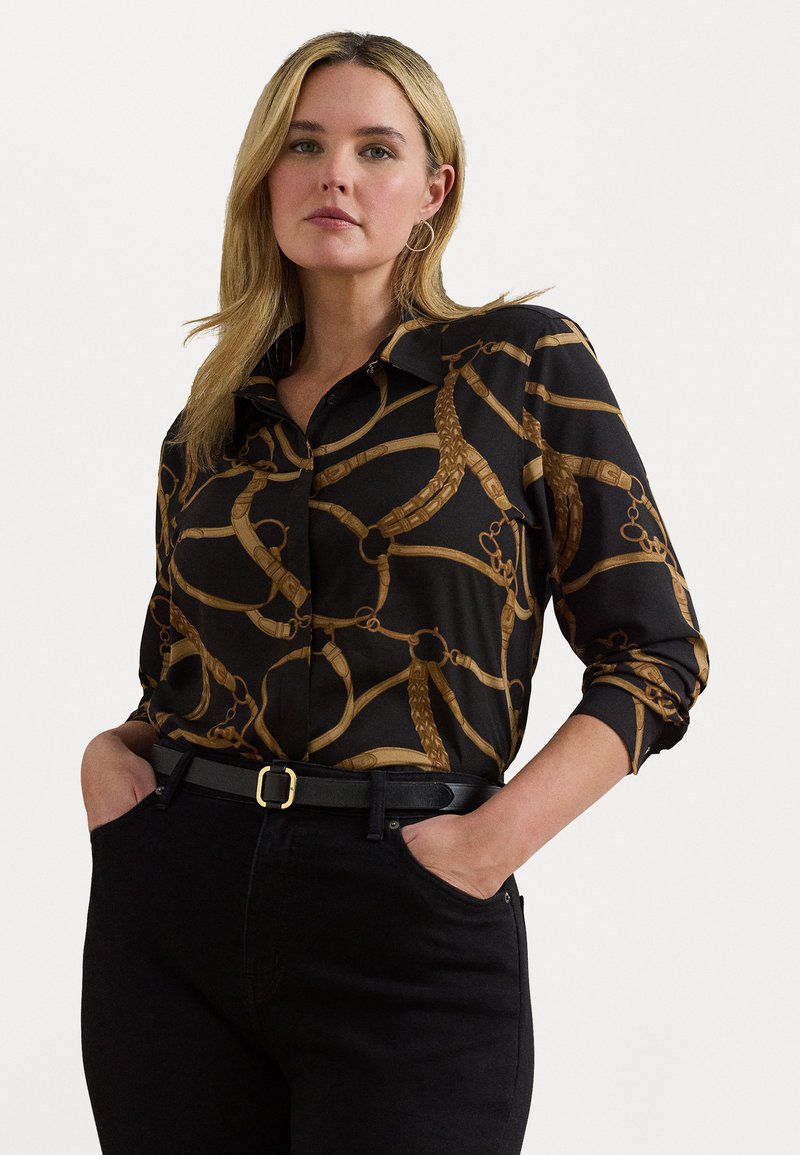 Svart knappskjorte med et gullkjede mønster, med langermede ermer rullet opp og spiss krage, kombinert med svarte jeans og et belte.
