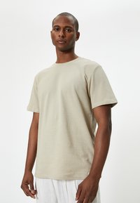 T-shirt beige a maniche corte realizzato in cotone morbido. Presenta un collo a giro e un orlo dritto, con una texture liscia e un design minimal.