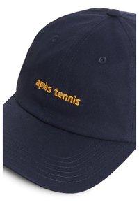 Temno modra bejzbolska kapa s ukrivljenim vizirjem, na sprednjem panelu pa je v oranžni vezenini napisan "apiès tennis".