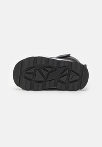 Black athletic shoe sole with textured rubber, featuring deep grooves and a multi-directional tread pattern for traction and durability.