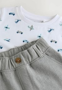 Chemise blanche pour enfant avec des véhicules bleus et gris et pantalon gris à taille élastique avec un bouton marron.