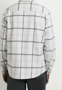 Camicia grigia chiaro con motivo a quadri, che presenta linee grigie scure e bianche. Design con bottoni e maniche lunghe, e orlo arrotondato.